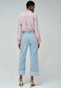Blusa de manga larga rosa claro combinada con jeans de tiro alto, de lavado claro y pierna ancha, con dobladillo doblado y bolsillos traseros. Sandalias de tacón.