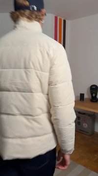 Geacă albă matlasată cu design cu cusături, văzută din spate. Țesătura pare moale și izolatoare, asortată cu blugi din denim închis la culoare.