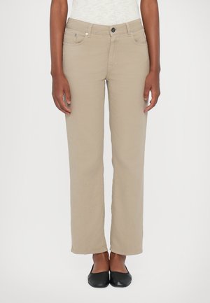 Beige rechttoe rechtaan broek met een platte voorkant, voorzakken en een metalen knoopsluiting; gecombineerd met zwarte ballerina's.