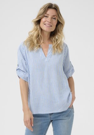 Camicia a righe blu e bianche con scollo a V e maniche arrotolate, realizzata in tessuto leggero. Abbinata a jeans in denim blu chiaro.
