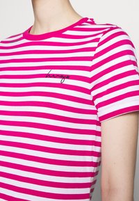 Camiseta de rayas rosas y blancas con cuello redondo. Cuenta con mangas cortas y un pequeño logotipo negro "hugo" en el pecho. Material de algodón.