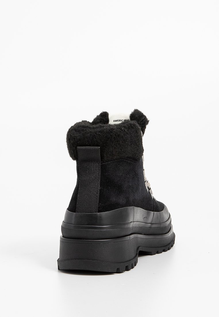 Czarne zamszowe kozaki za kostkę z miękkim czarnym kołnierzem, gumową podeszwą, pętlą z tyłu oraz dekoracyjnymi detalami. Teksturowana powierzchnia na całej długości.