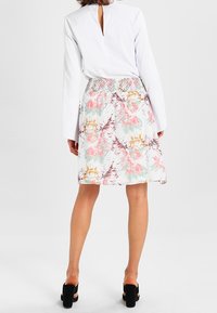 Vit blus med slits i ryggen, kombinerad med en blommig kjol i pastellfärger, med en rynkad midja och svarta klumpiga klacksandaler.