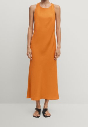 Ärmelloses orangenes Midikleid mit geknöpftem Schulterdetail, kombiniert mit schwarzen, offenen, flachen Sandalen vor einfarbigem Hintergrund.