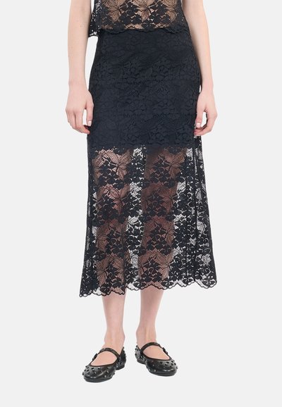 Zwarte kant maxi rok met bloemenpatronen, met een gelaagd ontwerp en een gegolfde zoom, gecombineerd met gestikte zwarte ballerina's.