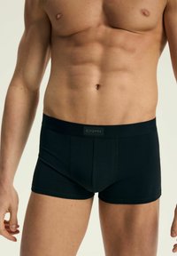Czarne bokserki wykonane z miękkiego materiału, z elastycznym pasem, który posiada metkę z nazwą marki. Tkanina ma gładką strukturę i dopasowany krój.