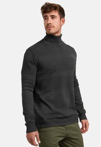 Maglione a collo alto in charcoal realizzato in tessuto a maglia testurizzato, con strisce orizzontali lisce a contrasto e polsini a costine, su uno sfondo chiaro.