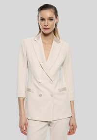 Blazer doppiopetto in beige chiaro, con una vestibilità sartoriale, rever a punta e due tasche frontali con dettagli accentuati discreti.