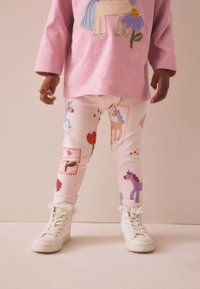 Rosa Baumwoll-T-Shirt mit Einhorn-Design, kombiniert mit weißen Leggings mit bunten Tier- und Blumenmustern, ergänzt durch weiße Turnschuhe.