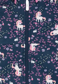 Mörkblå zip-up onepiece med tryck av en enhörning i rosa, vitt och lila, med blommiga och kaninaccentuerade detaljer genom hela tyget.