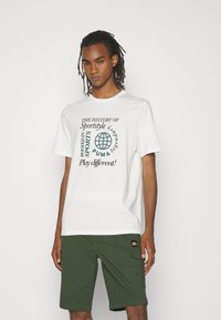 Witte t-shirt met groene grafische tekst, voorzien van een wereldbolontwerp. Gecombineerd met groene shorts, beide gemaakt van lichtgewicht stof.