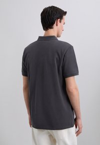 Polo de color gris oscuro hecho de algodón, con un cuello clásico y mangas cortas, con una textura suave y detalles de abertura lateral.