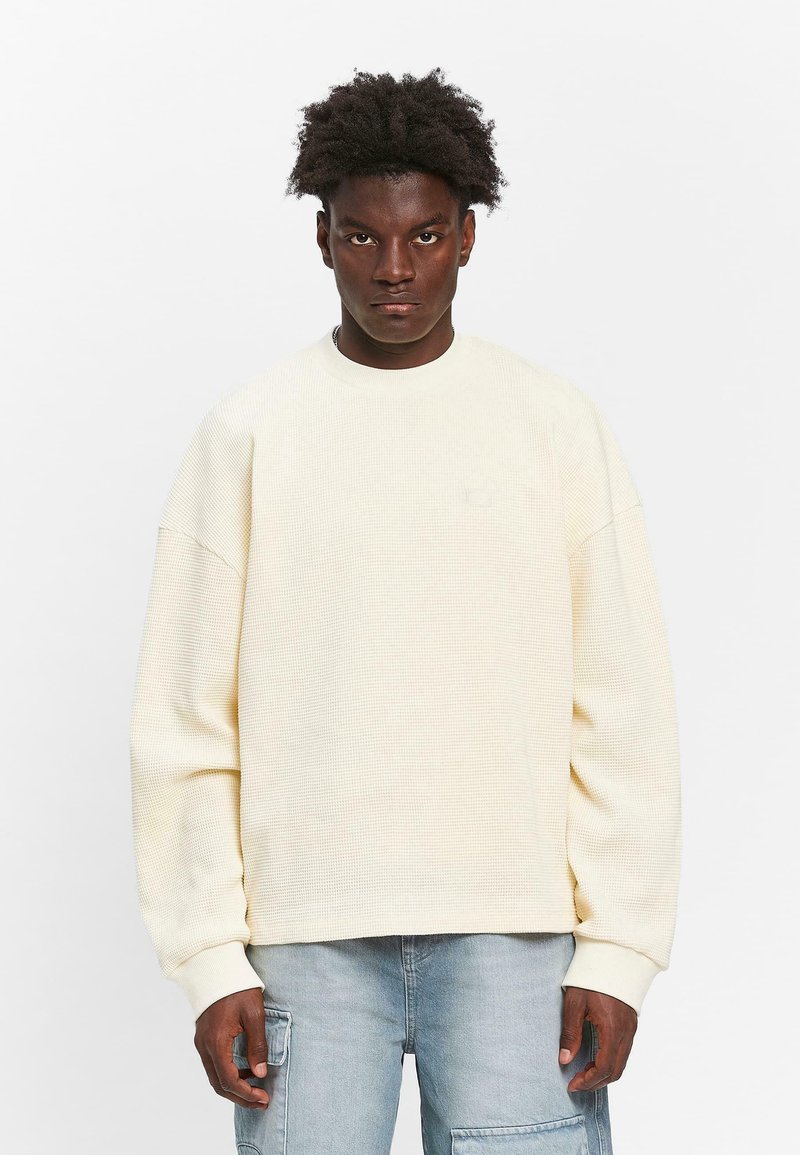 Crème-kleurig textuur sweatshirt met een ronde halslijn, verlaagde schouders en geribde manchetten, gedragen met lichtblauwe cargobroek.