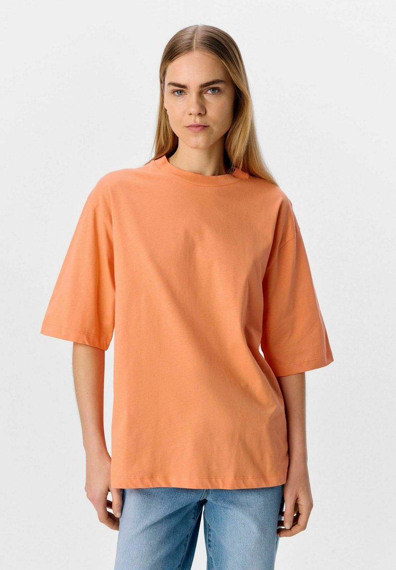 Camiseta de algodón naranja con un corte relajado, mangas cortas y un cuello redondo, acompa�ñada de pantalones vaqueros de color azul claro. Textura suave, diseño minimalista.
