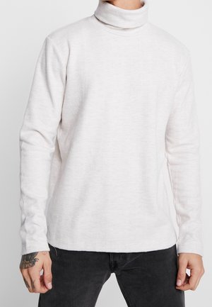Pull en col roulé gris clair avec une texture côtelée, des manches longues et une coupe décontractée, associé à un jean foncé pour un contraste.