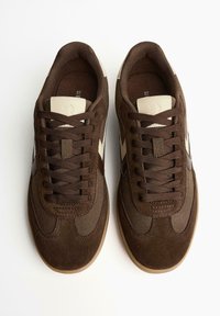 Une paire de baskets en daim marron à lacets avec des accents beiges, vue de dessus sur un fond blanc, taille marquée 37 à l'intérieur.