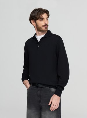 Maglione lavorato a maglia nero con collo a coste e pattina con tre bottoni. Presenta maniche lunghe e una vestibilità rilassata, abbinato a jeans grigi.