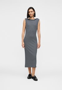 Φόρεμα με ρίγες από ελαστικό ύφασμα· διαθέτει καραβότρατα και αμάνικο σχέδιο. Το φόρεμα φτάνει μέχρι τους αστραγάλους και συνδυάζεται με μαύρα loafers.