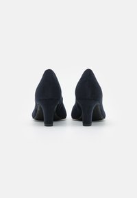 Zapatos de tacón alto de ante azul marino con un diseño afilado y un tacón bloque medio, que presentan una textura suave y una forma elegante.