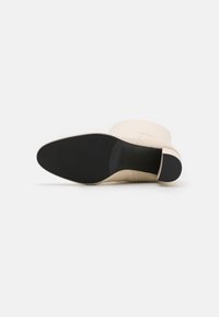 Botín beige hasta el tobillo con upper de cuero suave, punta redonda y suela de goma negra. El tacón es ligeramente elevado, lo que proporciona estabilidad.