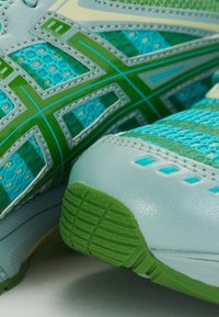 Sapatos desportivos com um esquema de cores em azul e verde, textura de malha e solas de borracha. Apresenta um design leve e detalhes de costura intrincados.