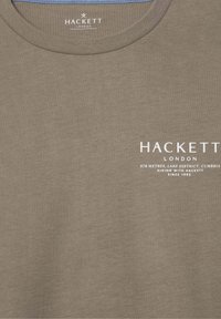 Taupe tričko s okrúhlym výstrihom a bielym logom "Hackett London" a textom "978 metrov, Lake District, Cumbria, turistika s Hackett od roku 1983."