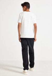 Vit bomull t-shirt med kort ärm, kombinerad med svarta denimbyxor. Ljusa sneakers kompletterar outfiten. Enkelt och minimalistiskt design.
