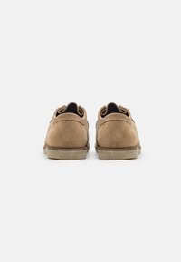 Zapatos de ante marrón con perfil bajo y acabado texturizado. La parte trasera muestra un tacón redondeado y detalles de costura minimalistas.