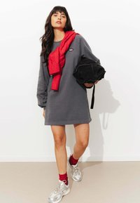 Robe sweat gris avec manches longues, associ�ée à une écharpe en maille rouge et un sac noir. Des baskets argentées et des chaussettes rouges viennent compléter le look.