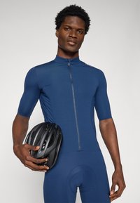 Marine sykkeldrakt med korte ermer og glidelås foran. Modellen holder en svart sykkelhjelm. Glatt stoff og tettsittende design.