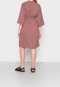 Pink floral dress with short, bell sleeves, elastic waist, and a relaxed fit. Worn with brown strappy sandals. Smooth fabric texture.