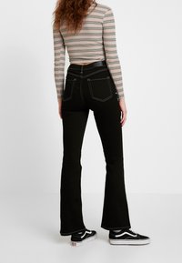 Svarta utsvängda jeans med kontrasterande vit söm, med hög midja och bakfickor. Kombineras med svarta och vita sneakers.