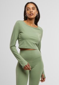 Világos zöld, hosszú ujjú, rövidített fazonú top, sima anyagból készült, kerek nyakkivágással és finom varrási részletekkel, amelyhez illő, magas derekú leggings tartozik.