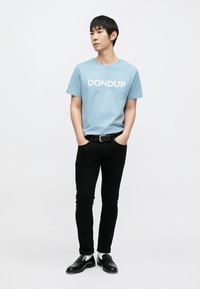 Ανοιχτό μπλε κοντομάνικο t-shirt με το λογότυπο "DONDUP" τυπωμένο σε λευκό, συνδυασμένο με στενά μαύρα παντελόνια και μαύρα παπούτσια.