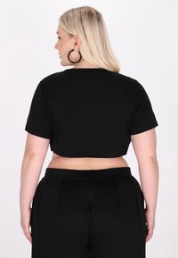 Sort cropped t-shirt med korte ærmer, der har et enkelt design og en blød tekstur. Sammen med højtaljede sort bukser.