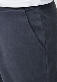 Navy blue sweatpants with a smooth, textured fabric; features a side pocket and an elastic waistband for comfort.
