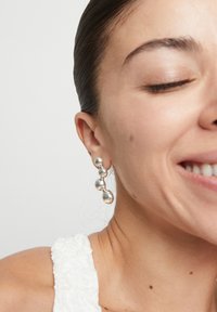 Boucles d'oreilles pendantes en argent avec des formes sphériques variées et des textures polies, mettant en valeur un design moderne et géométrique.