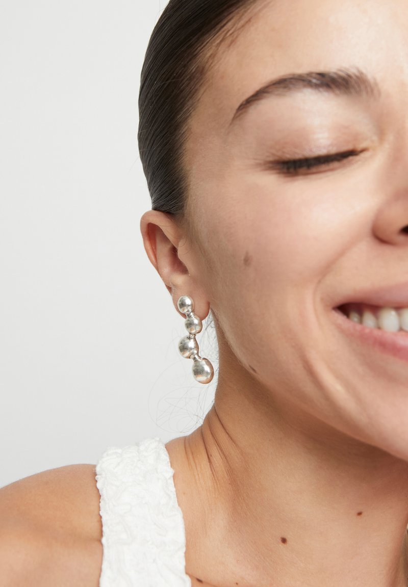 Boucles d'oreilles pendantes en argent avec des formes sphériques variées et des textures polies, mettant en valeur un design moderne et géométrique.