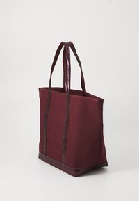 Bordeauxfarbene Stofftasche mit glänzenden, dunkelvioletten Griffen und Besatz. Rechteckige Form, strukturiertes Design, keine sichtbaren Muster oder Akzente.