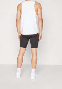 Top atlético blanco sin mangas, combinado con pantalones cortos ajustados negros. El atuendo se complementa con zapatillas blancas y calcetas atléticas visibles.