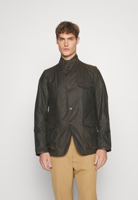 Dark green waxed cotton jacket with a high collar, four front pockets, and button closures, featuring a slightly textured finish.