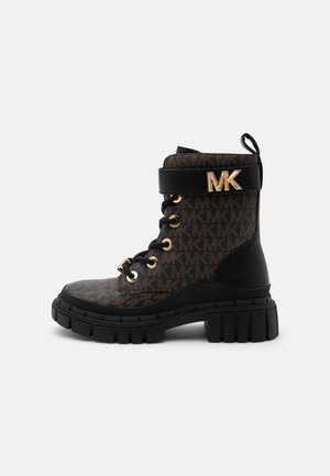 Botte montante marron et noire avec semelle noire épaisse, œillets dorés, laçage à l'avant, bride avec logo doré "MK", et motif de marque sur le tissu.