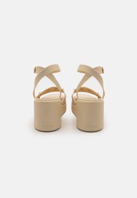 Sandales à plateforme beiges avec des brides croisées, fabriquées en matériau ressemblant au caoutchouc, avec une semelle intérieure texturée et un talon de marque.