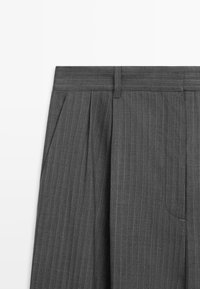 Pantalon gris foncé à fines rayures avec plis et passants de ceinture, montré de la taille jusqu'au milieu de la cuisse sur fond blanc.