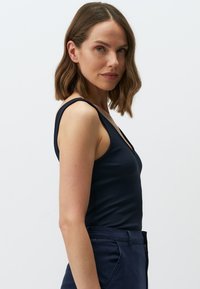 Canottiera a righe blu navy con spalline sottili e scollatura a V profonda, abbinata a pantaloni alti blu navy scuri. Tessuto morbido e design aderente.