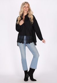 Camicia nera a maniche lunghe con orlo in pizzo, abbinata a jeans azzurri chiari e stivali neri con tacco. Presenta una vestibilità rilassata.