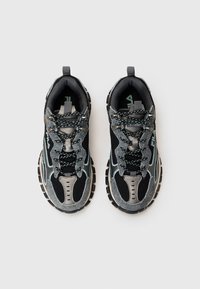 Scarpe sportive nere con parte superiore in mesh e suede, suola in gomma e dettagli riflettenti. I lacci presentano motivi colorati intrecciati.