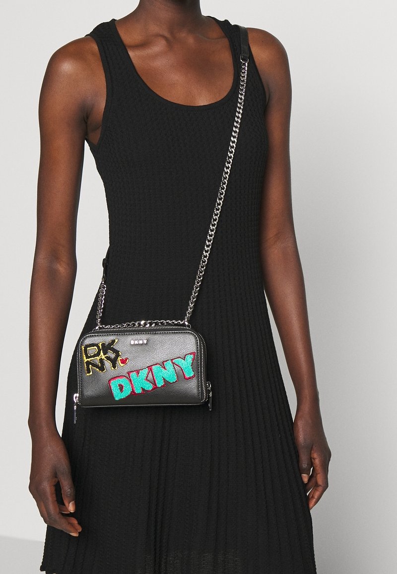 Borsa a tracolla nera in pelle sintetica con tracolla a catena intrecciata, caratterizzata da un ricamo colorato del logo DKNY e scomparti con zip.