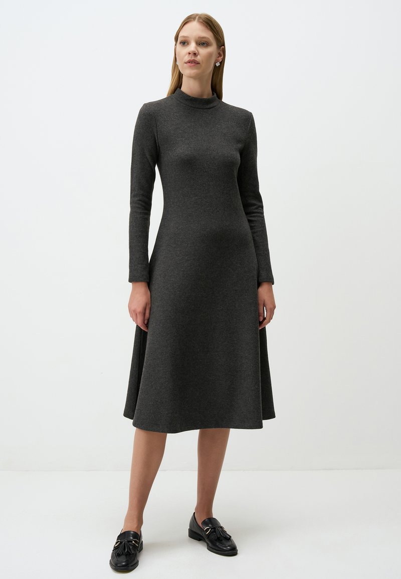 Graues, langärmeliges Kleid mit höherem Kragen, ausgestelltem Rock und glatter Textur, kombiniert mit schwarzen Slippern mit dekorativen Akzenten.
