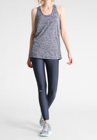 Leggings deportivos azul marino y una camiseta sin mangas gris jaspeada. Las leggings tienen un logo, mientras que la parte superior tiene un escote redondeado y un corte holgado. Unas zapatillas grises completan el conjunto.